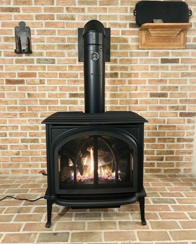 A wood stove with the door open and a pot on top of it.