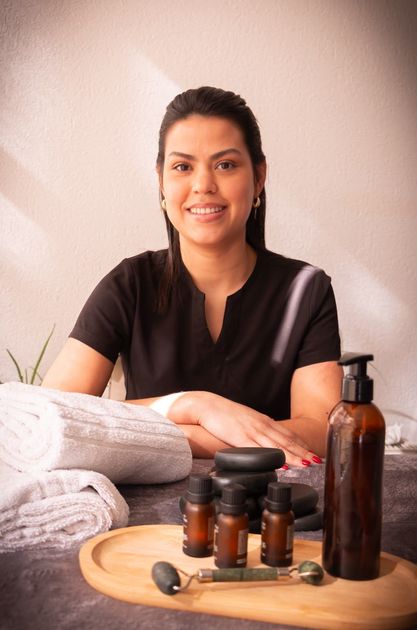 Persona sonriente en una camilla de spa con toallas, frascos de aceites esenciales y utensilios de masaje