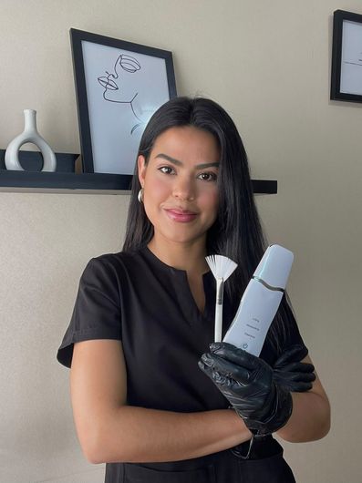 Persona con uniforme y guantes negros sosteniendo un dispositivo blanco en una sala de spa