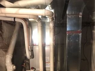 Basement with exposed pipes, ductwork, and bright light coming through a window