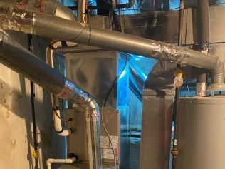 Industrial pipes and metal tanks in a mechanical room with a blue tarp in the center.