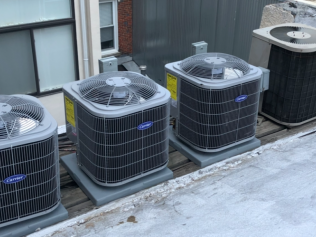 Three outdoor air conditioning units beside a building wall on a concrete pad