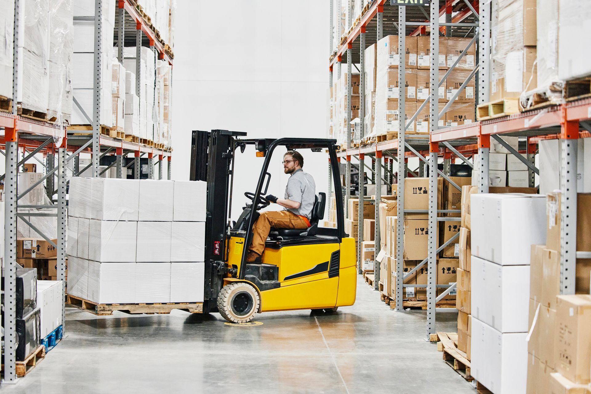 Warehouse worker driving forklift carrying pallet of goods.