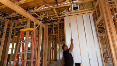 Two technicians installing kitchen cabinets in a bright, modern kitchen, using tools and a laser level.