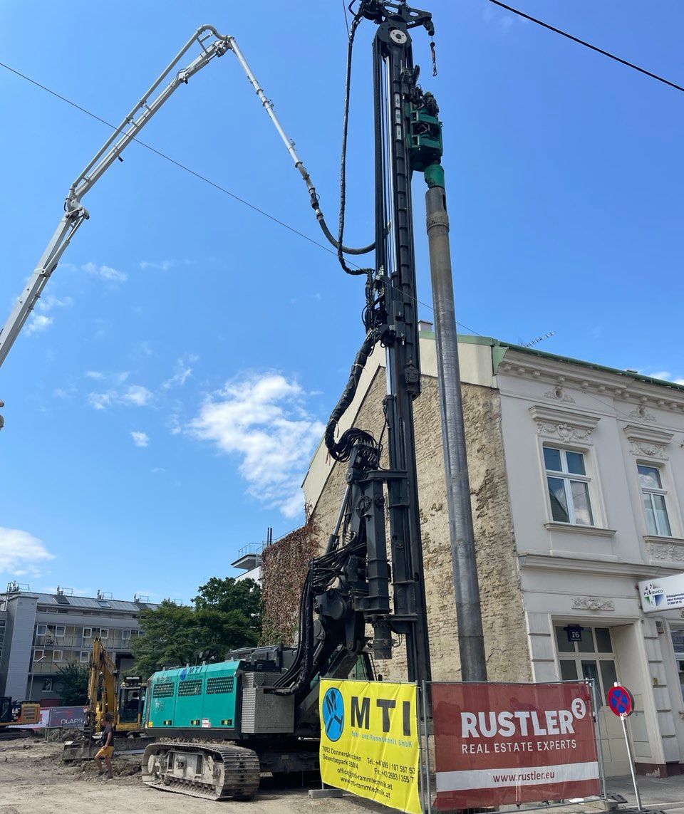 Baustelle mit Bohrmaschine und Betonpumpe neben einem Gebäude. Strahlend blauer Himmel.