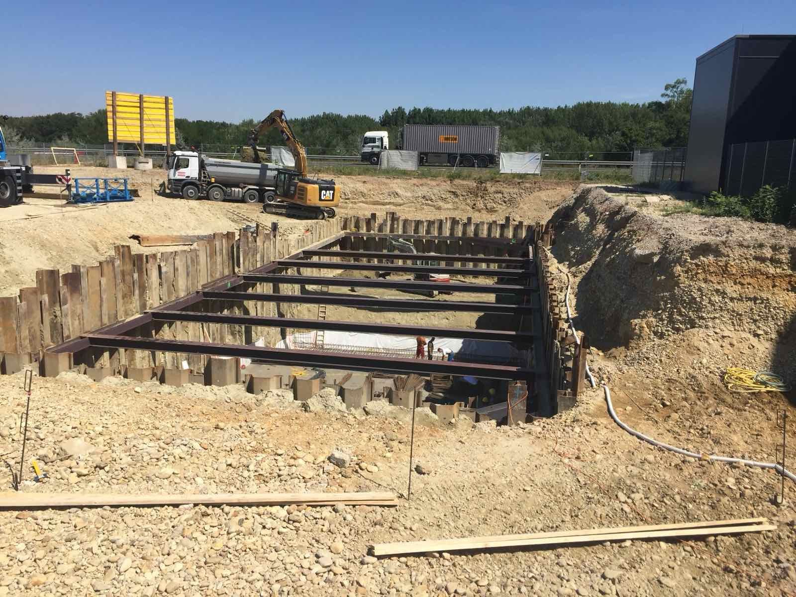 Baustelle mit einem Bagger, der eine mit Holz- und Metallstützen verstärkte Grube aushebt.