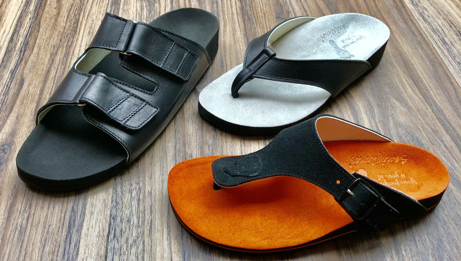 Drie zwarte en oranje sandalen op een houten ondergrond.