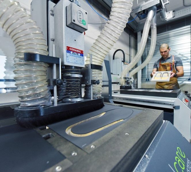 Een man bedient een CNC-machine en bewerkt materiaal. Werkplaatsomgeving met stofafzuigslangen.