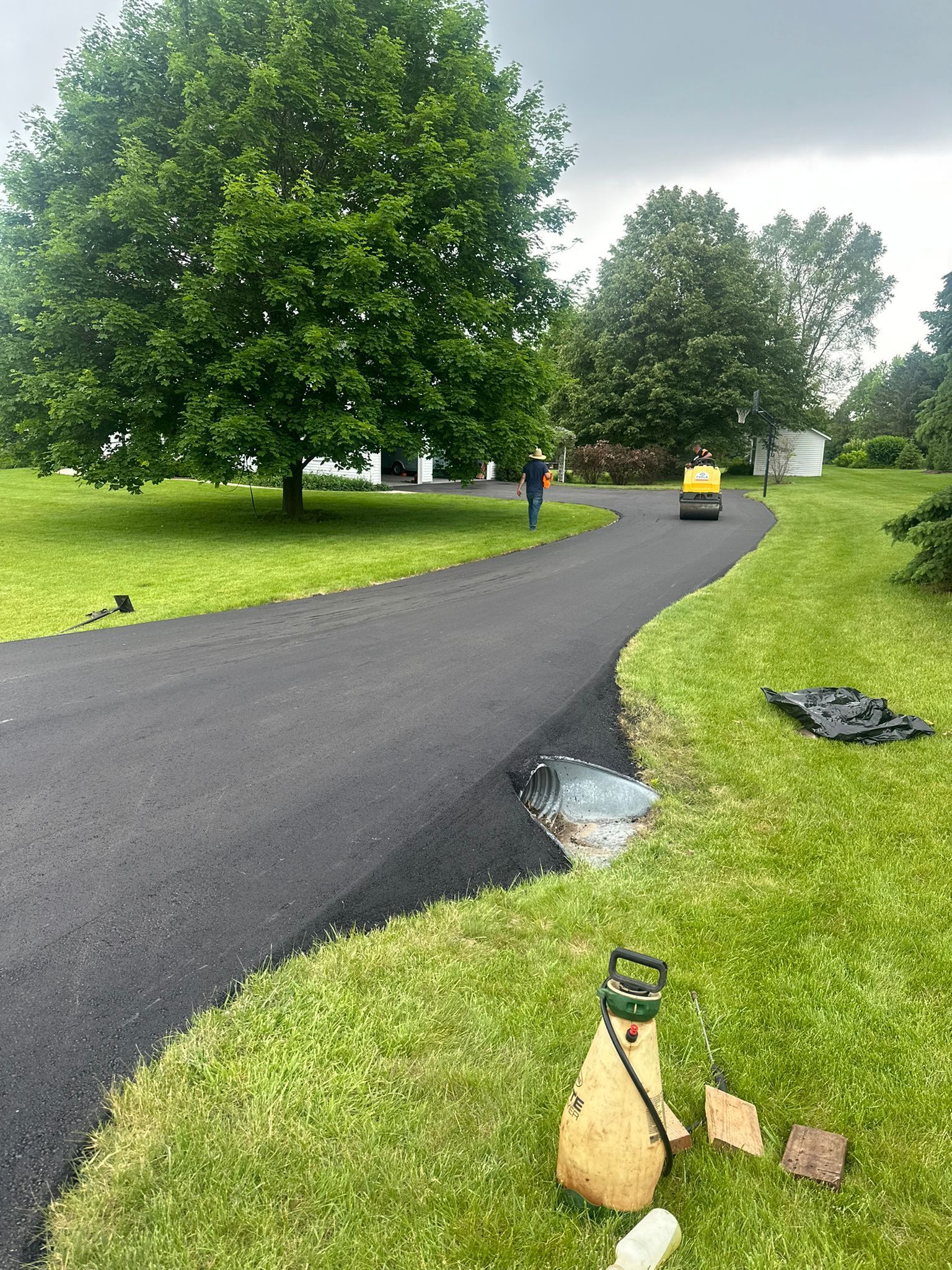 Paved, winding driveway through a grassy yard. A small vehicle is compacting the asphalt.