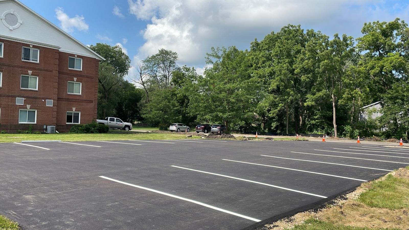 Newly paved parking lot with white parking space lines in front of a brick building and trees.