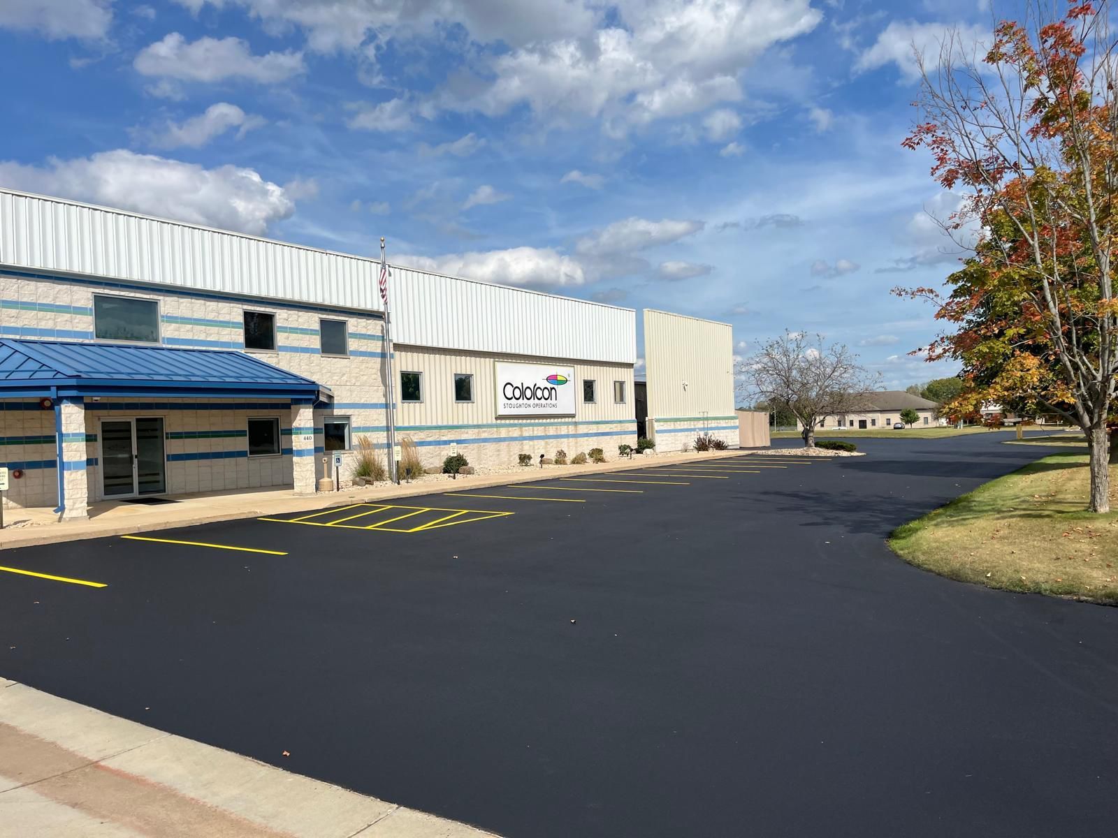 Exterior of a business building with a blue awning, asphalt parking, and a cloudy sky.