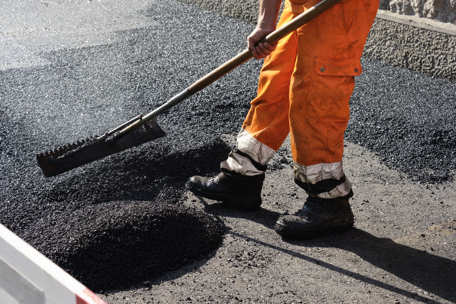 Construction worker spreads hot asphalt with a rake, leveling fresh pavement. Construction worker spreads hot asphalt with a rake, leveling fresh pavement.