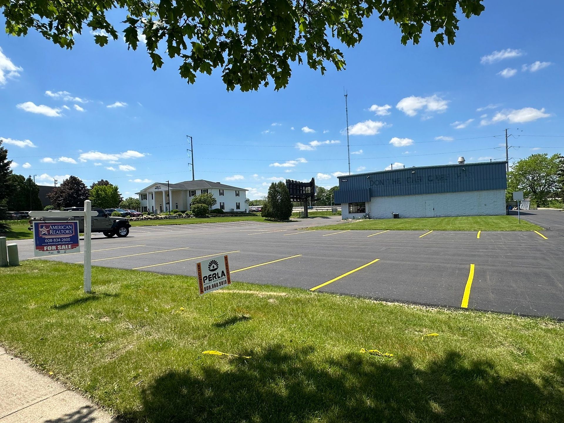 Exterior view of an empty parking lot on a sunny day. Building, sign, and grassy area visible.