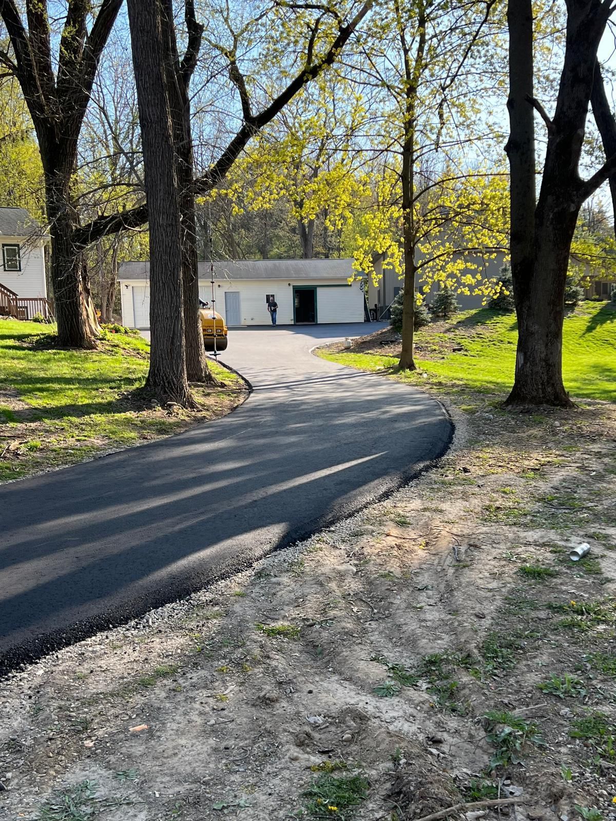 Paved driveway curves toward a white garage building, framed by trees and grassy lawn.