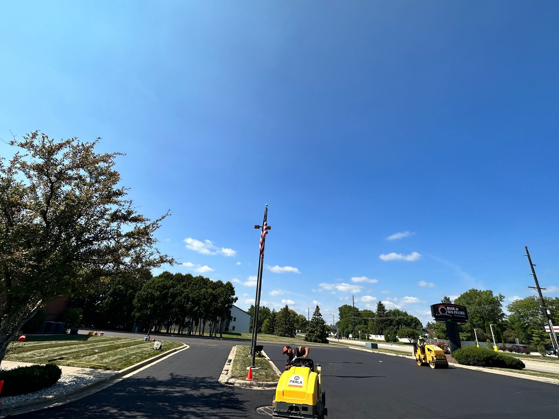 Asphalt paving in progress on a sunny day. Two compacting machines work on a newly paved road.