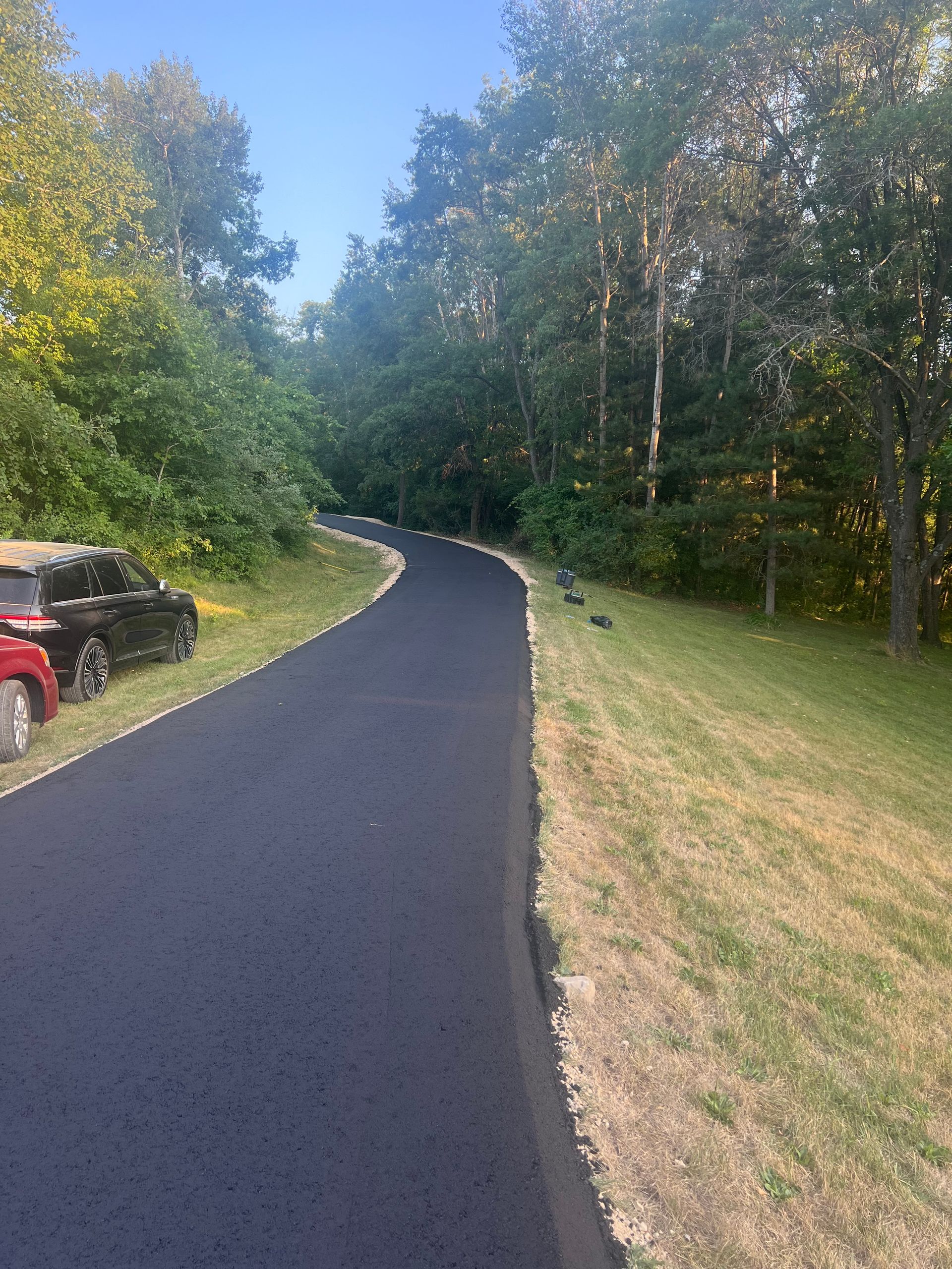 Black asphalt path curves through trees and alongside grassy bank.