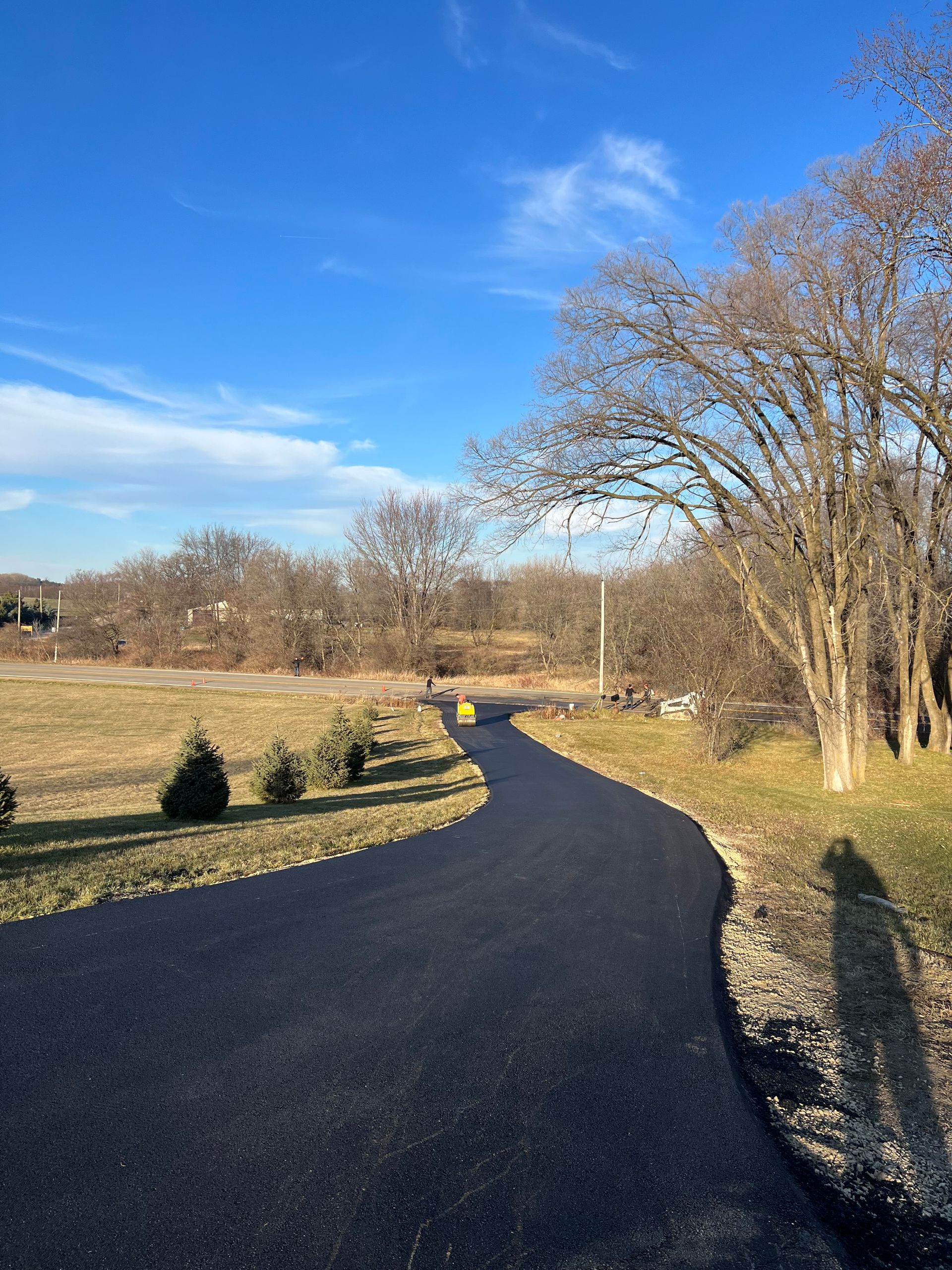 A newly paved, winding asphalt driveway curves through a landscape on a sunny day.