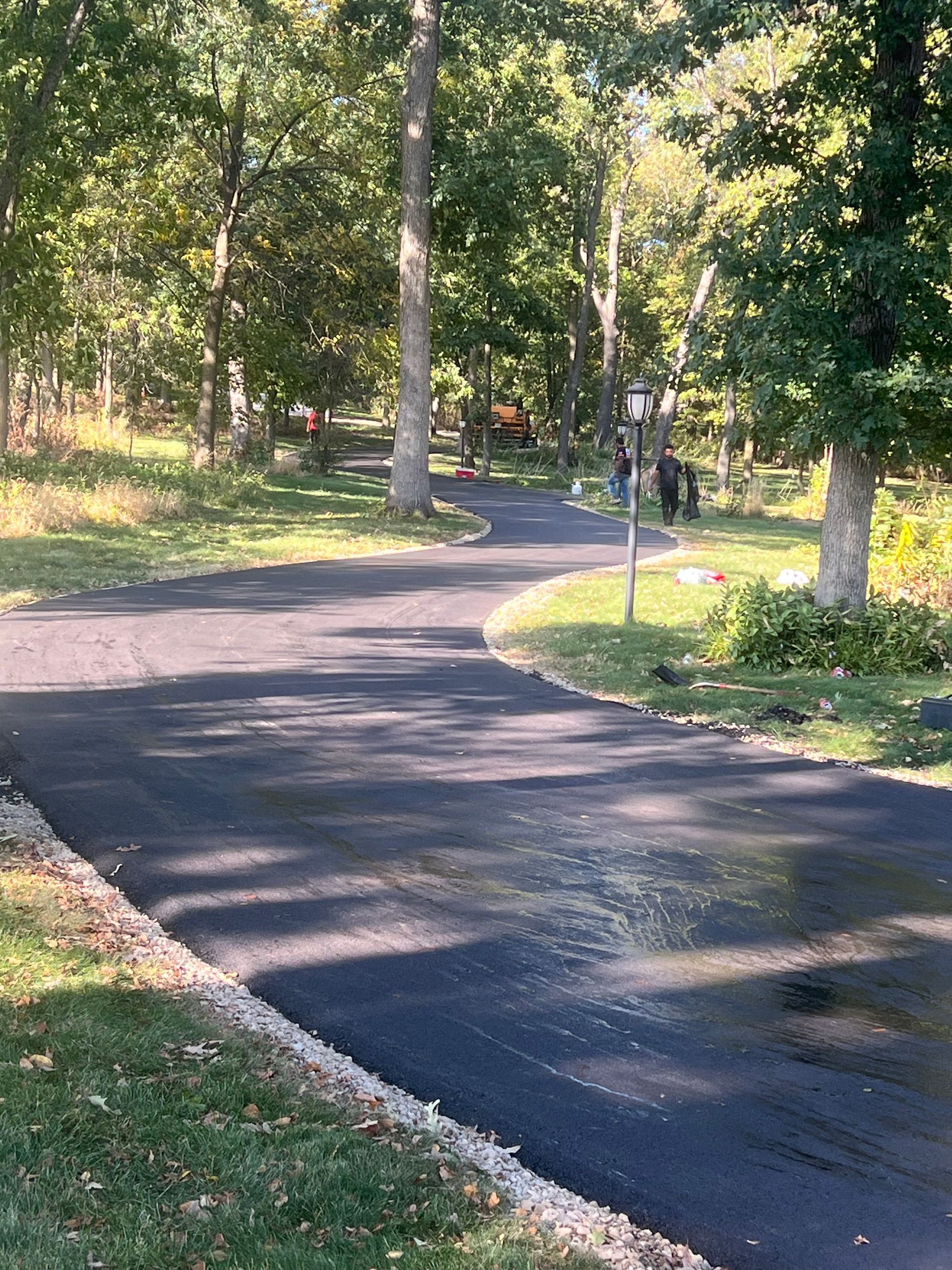 Newly paved asphalt driveway curves through a wooded area.