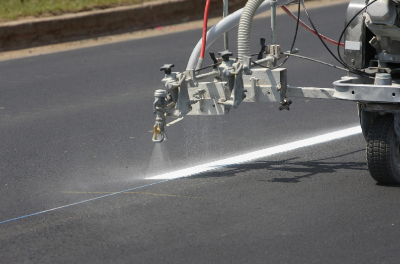 Road painting machine spraying a white line on dark asphalt.