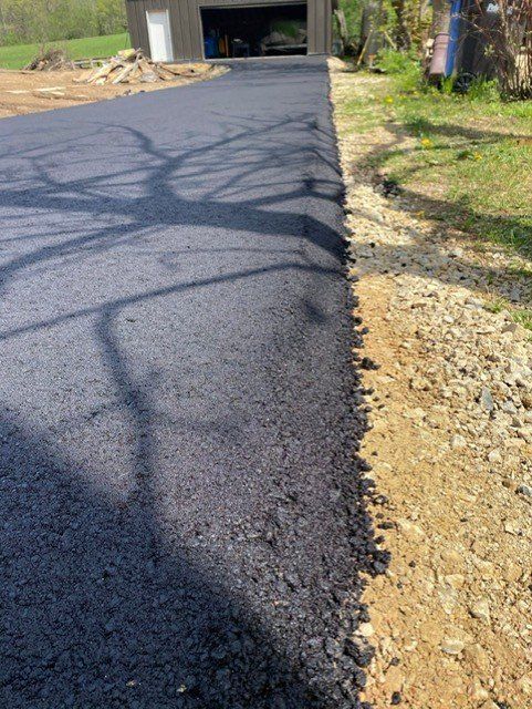 Newly paved asphalt driveway next to a gravel and dirt edge, leading to a garage.