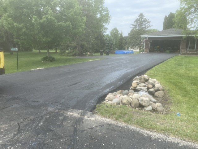 Newly paved asphalt driveway leading to a garage; landscaping on the right.