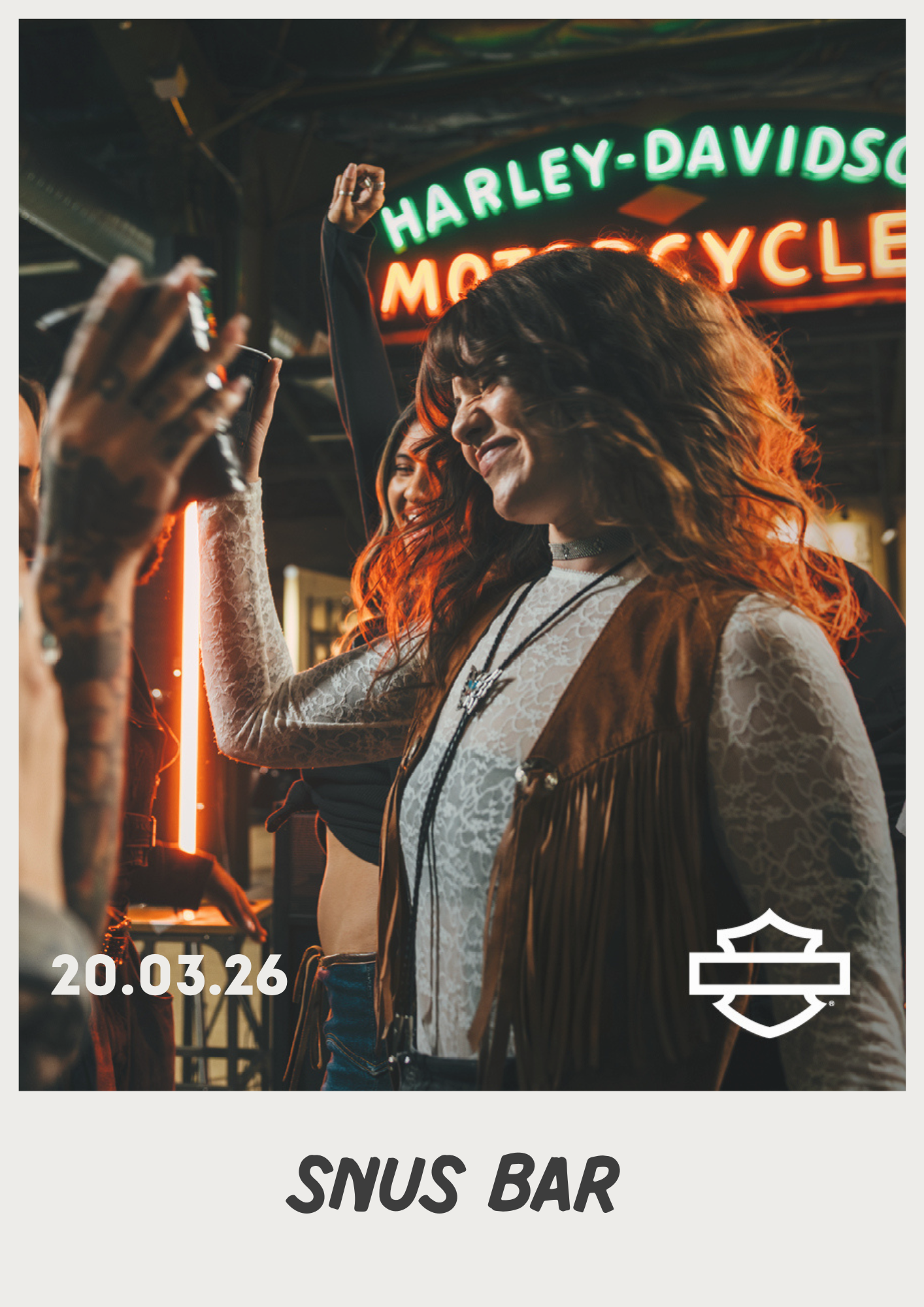 In einer schwach beleuchteten Bar jubeln Menschen unter einem leuchtenden Harley-Davidson-Neonschild mit Logo in der Ecke.