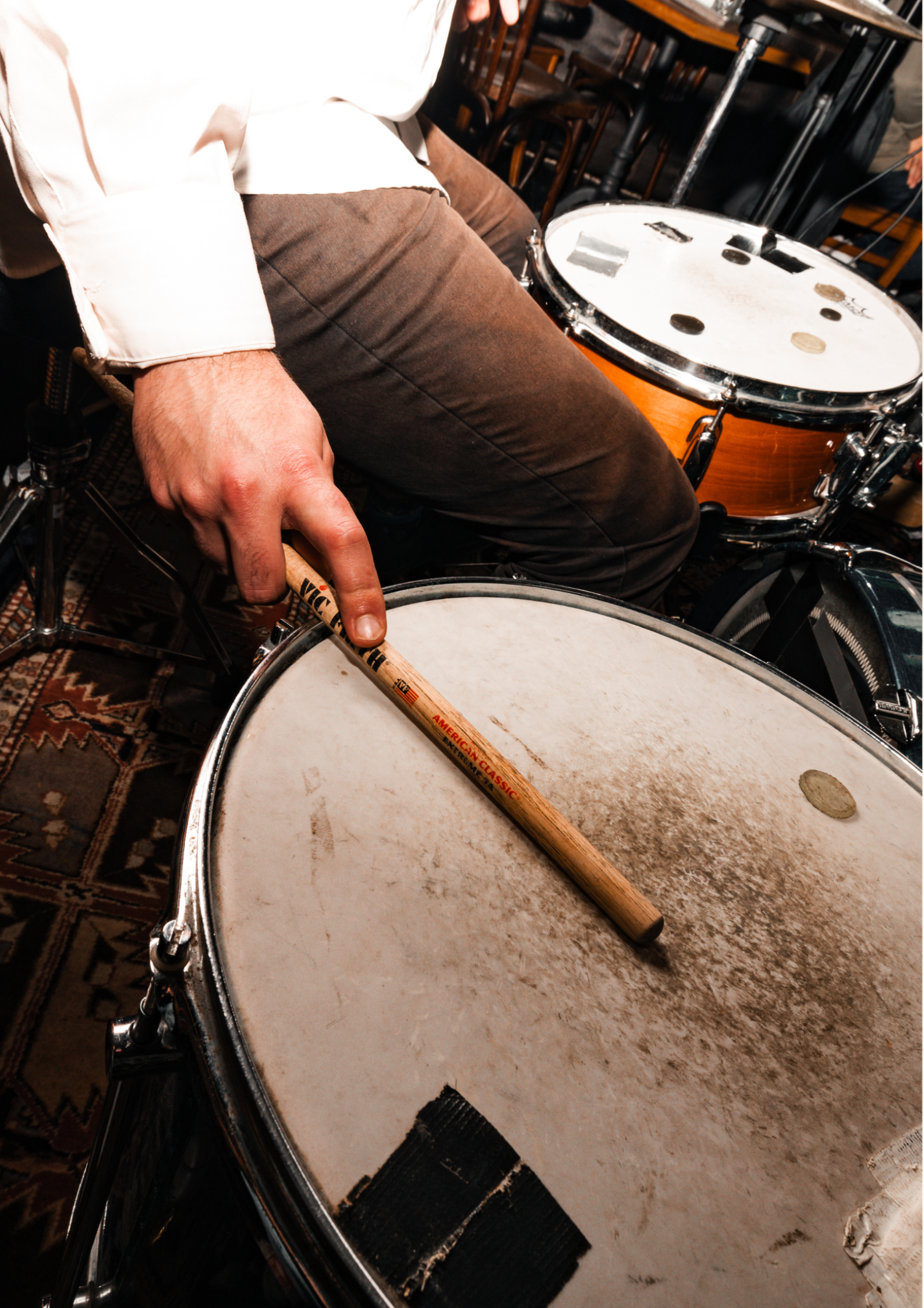 Nahaufnahme der Hand eines Schlagzeugers, der einen hölzernen Trommelstock gegen das Fell einer Snare-Drum hält; in der Nähe ist eine Tom-Drum zu sehen.