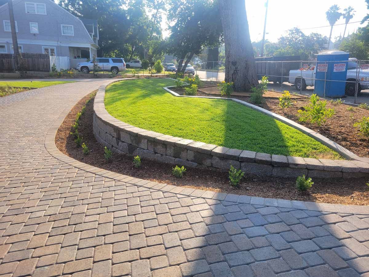 Brick driveway curving around a small lawn with a low retaining wall; light house in the background.