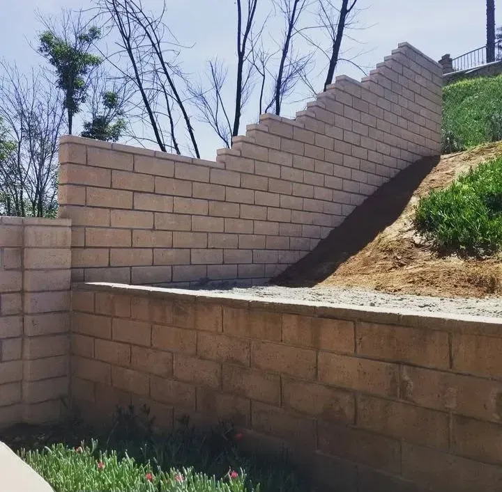 Tan brick retaining walls on a hillside, with a stepped section, in a sunny outdoor setting.