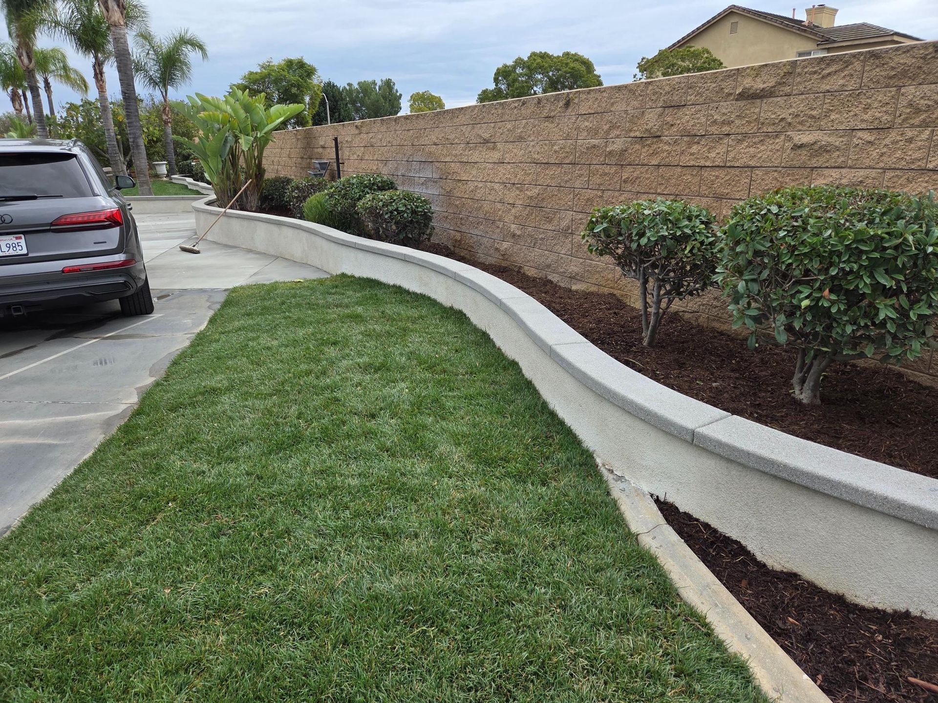Green lawn with concrete curb, bushes, and a textured retaining wall.