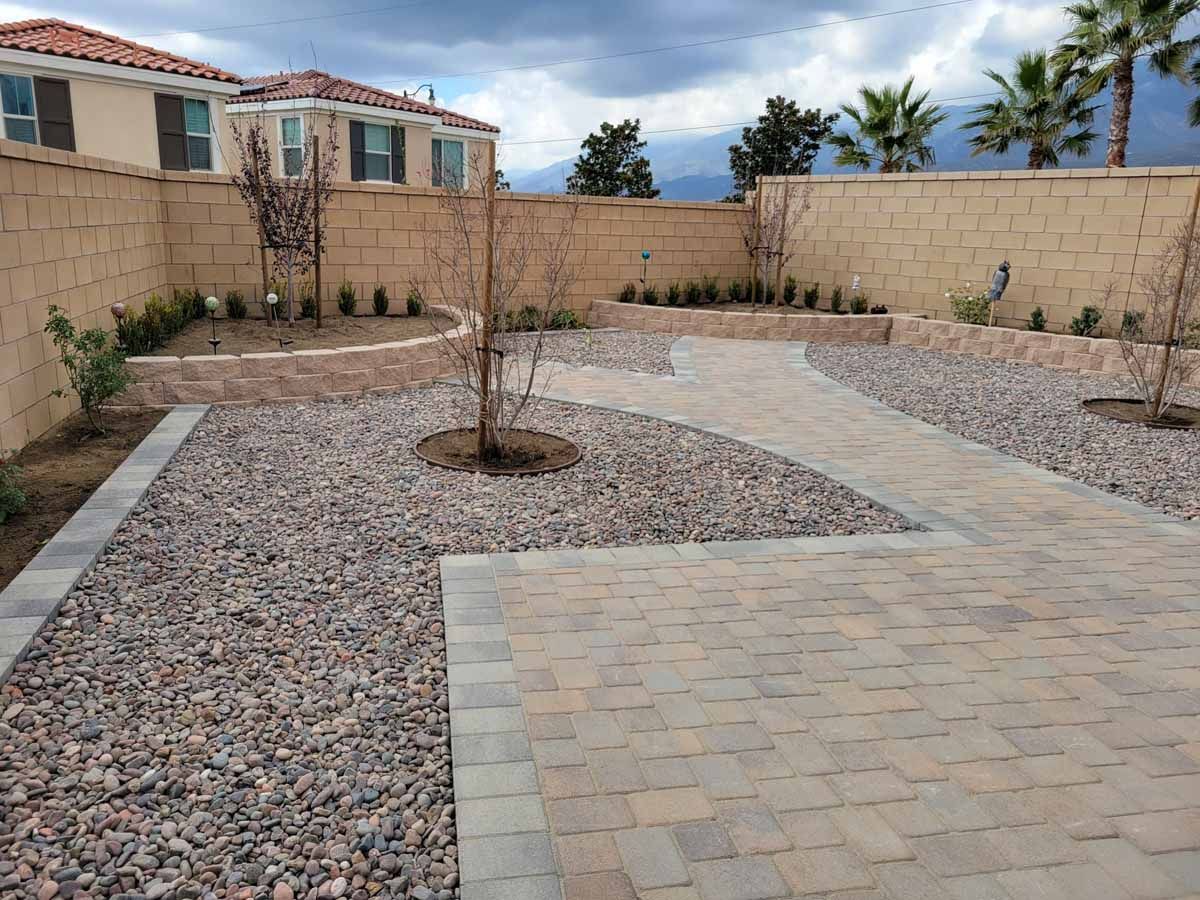 Backyard with stone patio, gravel, brick walls, and landscaping.