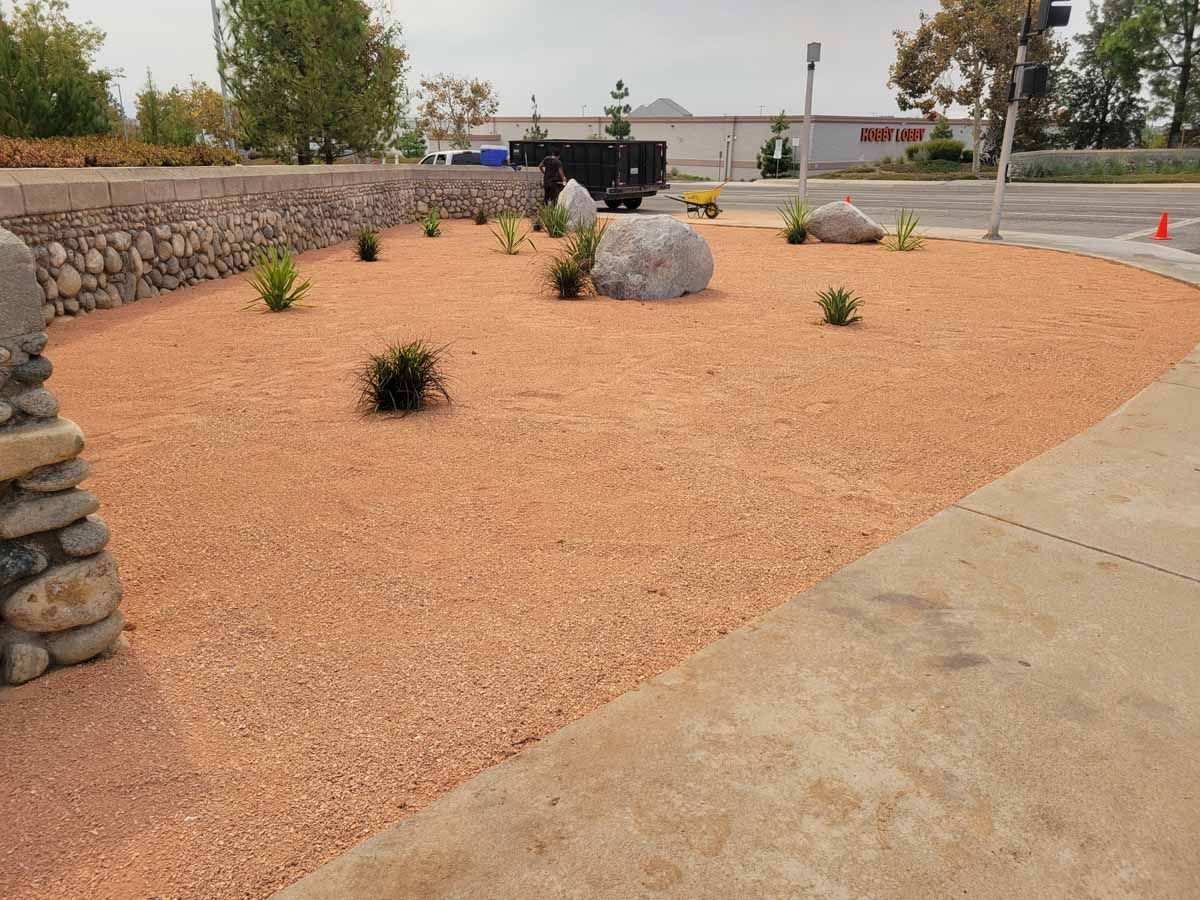 Landscaped area with reddish gravel, plants, rocks, and a stone wall in front of a business.