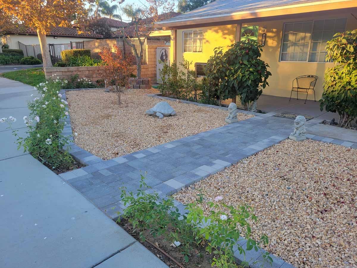 Stone pathway leading to a yellow house with rock landscaping and blooming rose bushes.