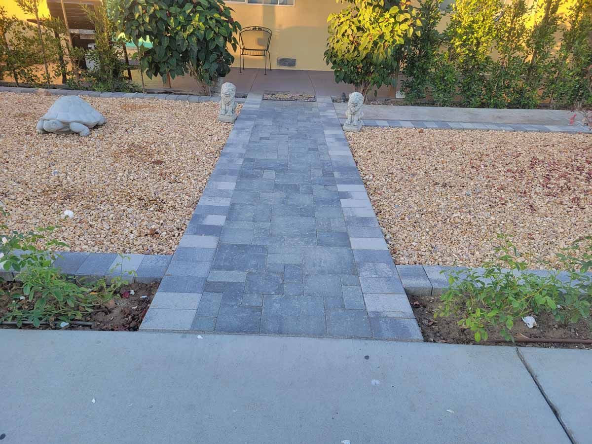 Brick walkway leading to a house entrance, flanked by gravel beds and greenery.