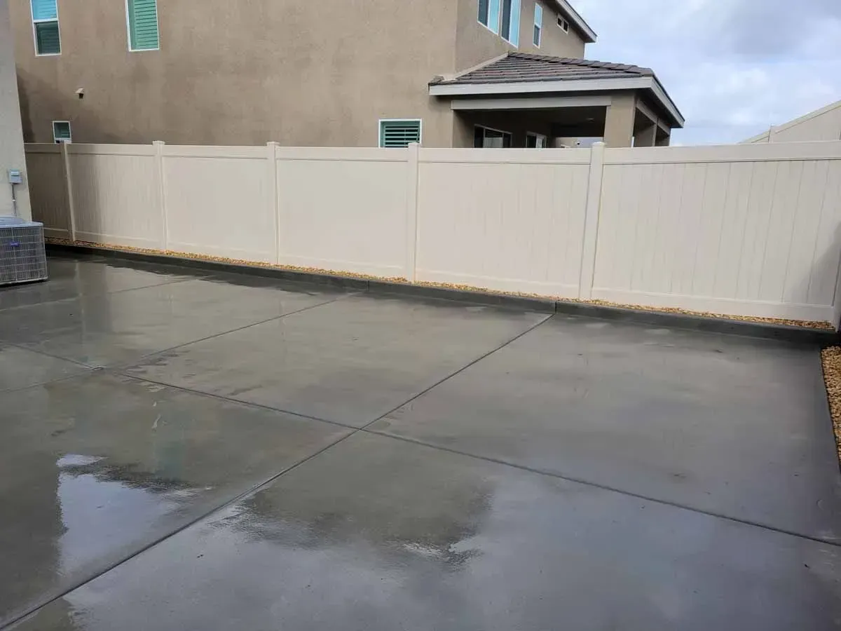 Backyard concrete driveway with tan vinyl fence, under overcast sky.