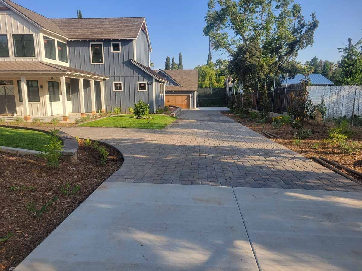 A house with a gray exterior and a brick driveway on a sunny day.