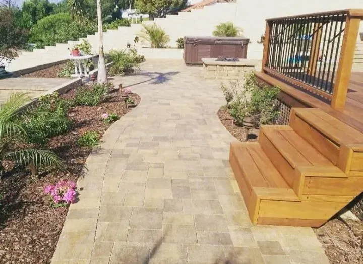 Stone path leading to deck and hot tub in a sunny backyard.
