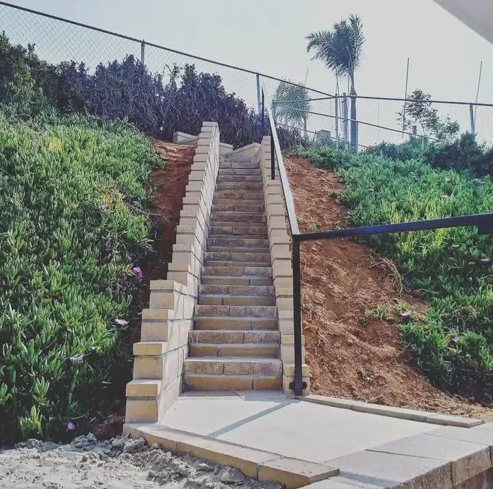 Stone stairs leading up a grassy hill, with a black railing and fence.
