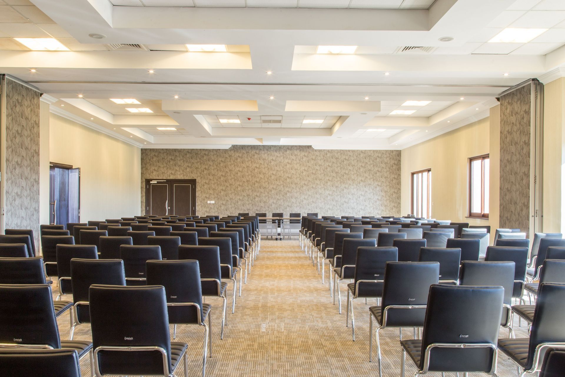 Empty conference room with rows of black chairs facing a podium and projector screen.