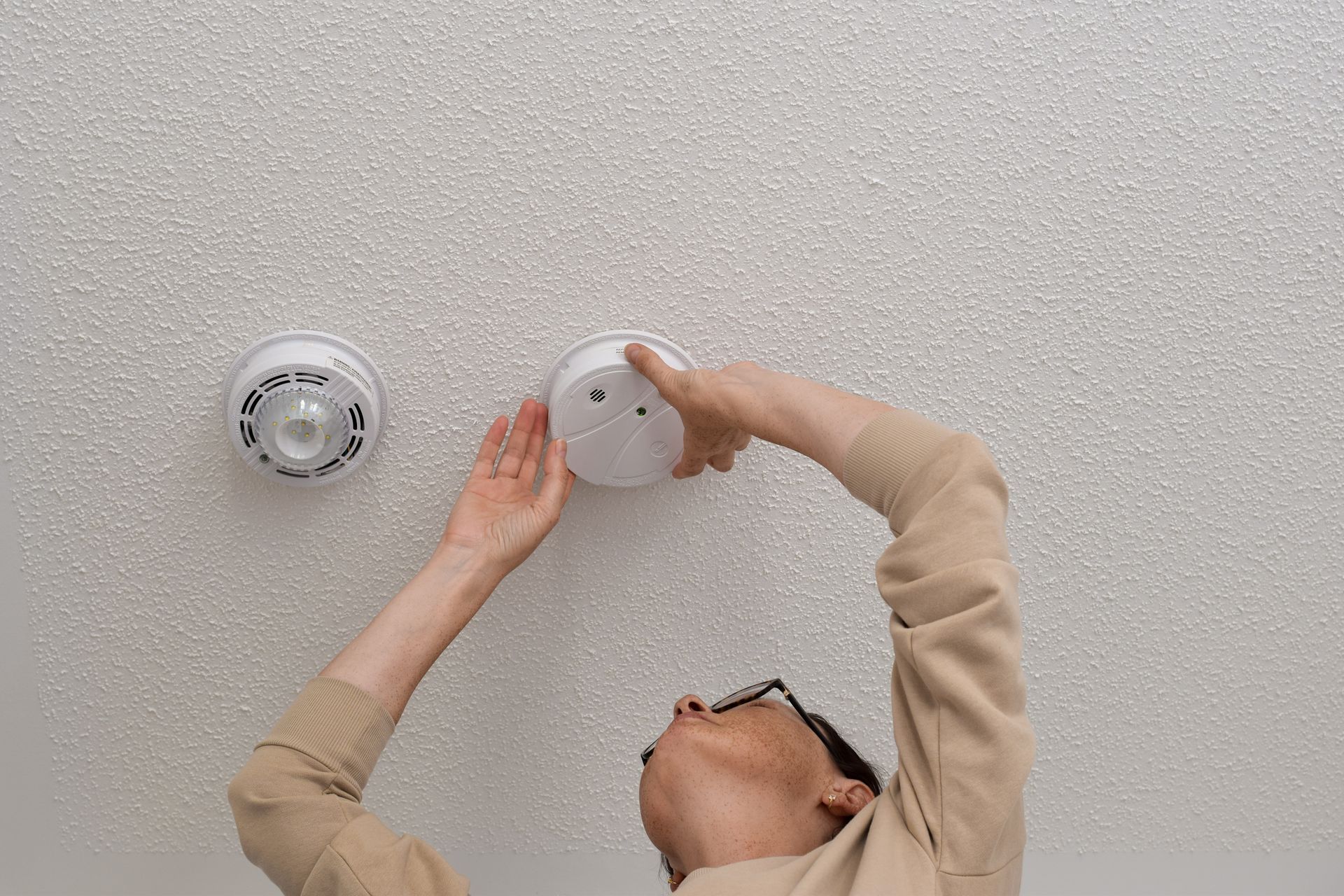Person Installing a Smoke Detector on a Textured White Ceiling — Jade Fluerty Electrical In Tinana, QLD