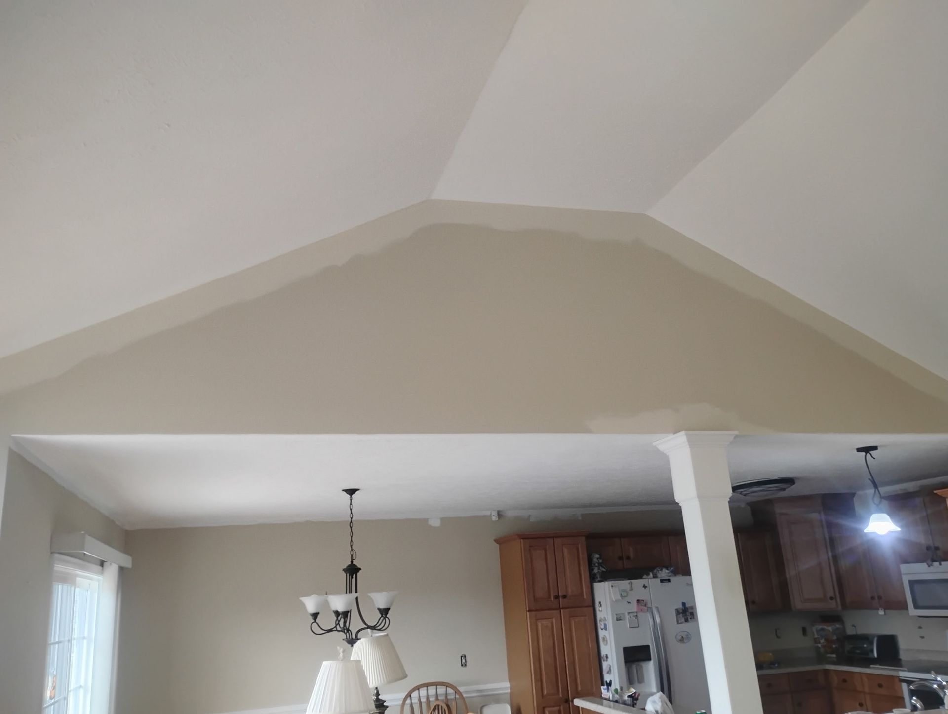 A tan, vaulted interior wall undergoing a partial paint job, showing a darker color transition against white ceilings.