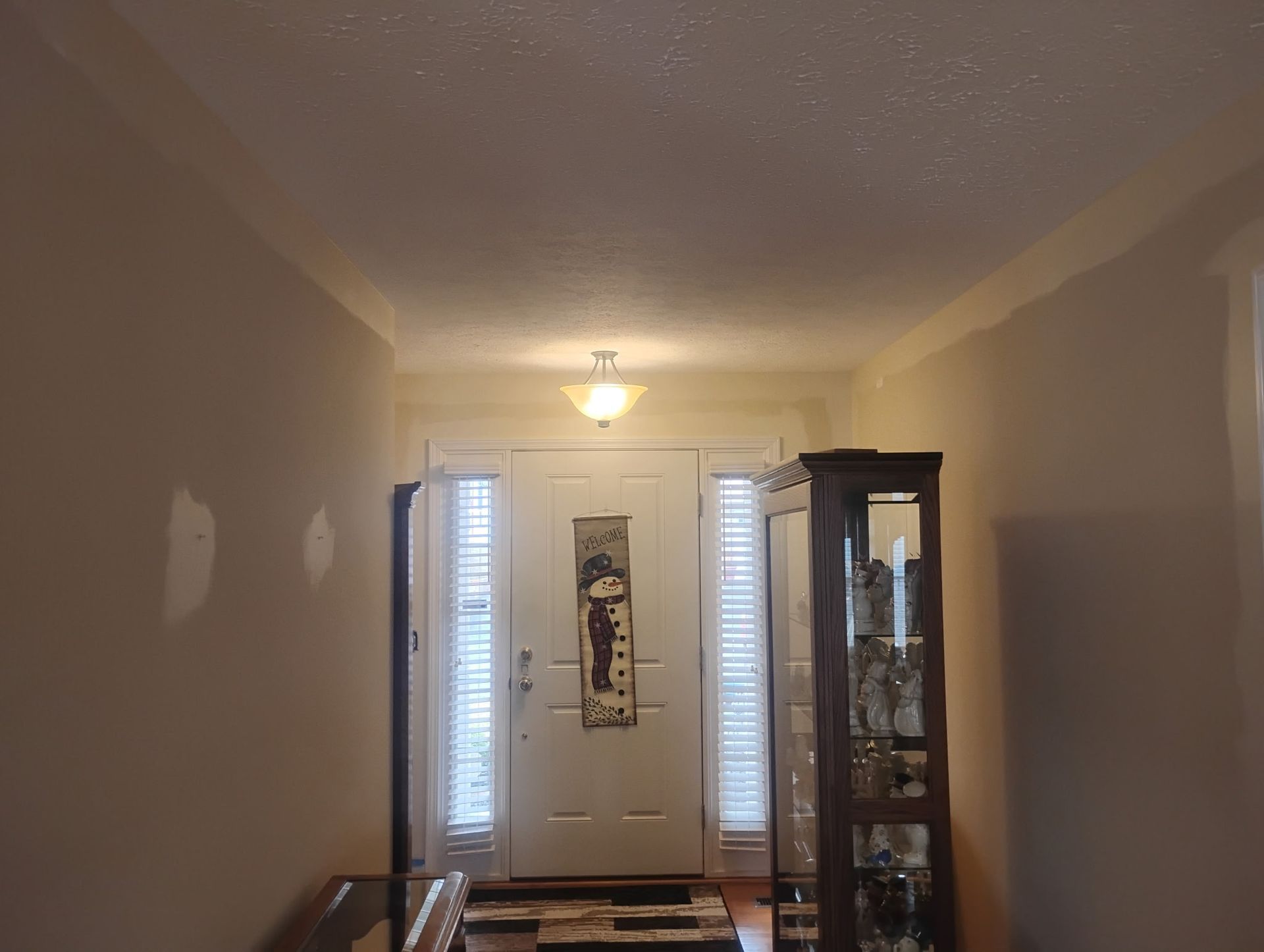 A hallway with light-colored walls leads to a white front door with sidelight windows, a hanging light, and a display case.