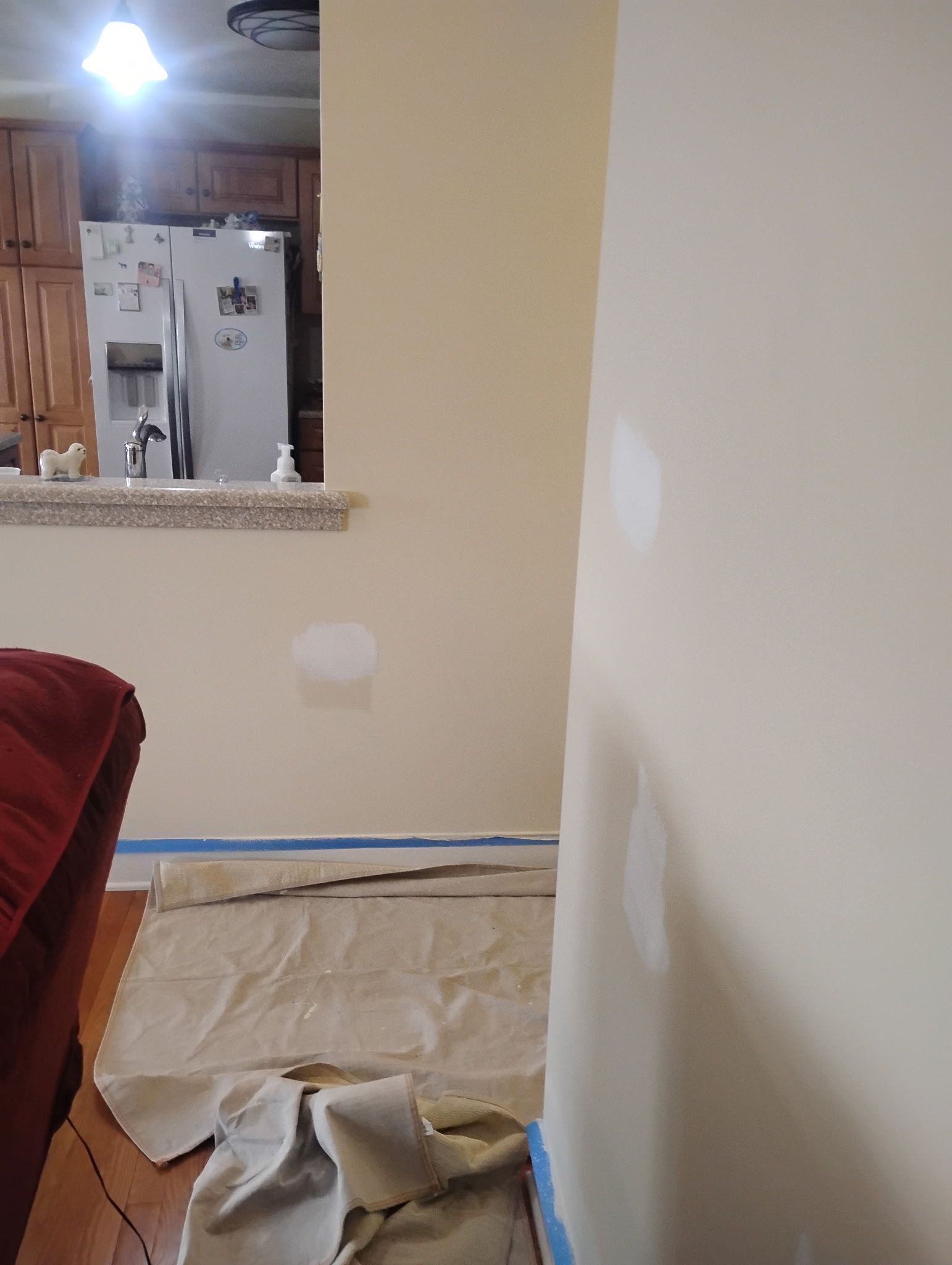 A beige wall with several white spackle patches, prepared for painting with floor protection and blue painter's tape.