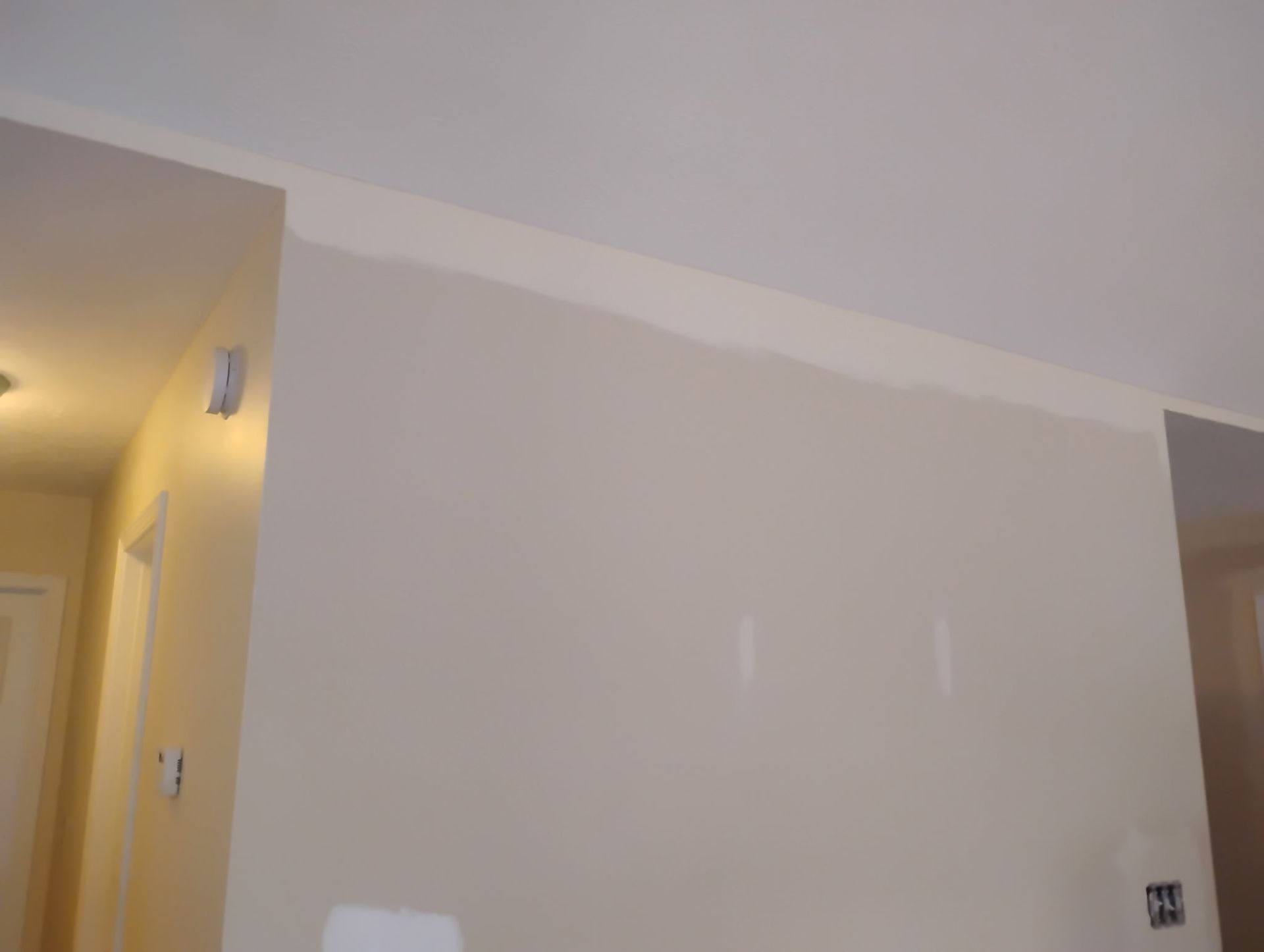 An interior wall with a freshly painted light beige coat that shows a visible lighter strip near the ceiling.