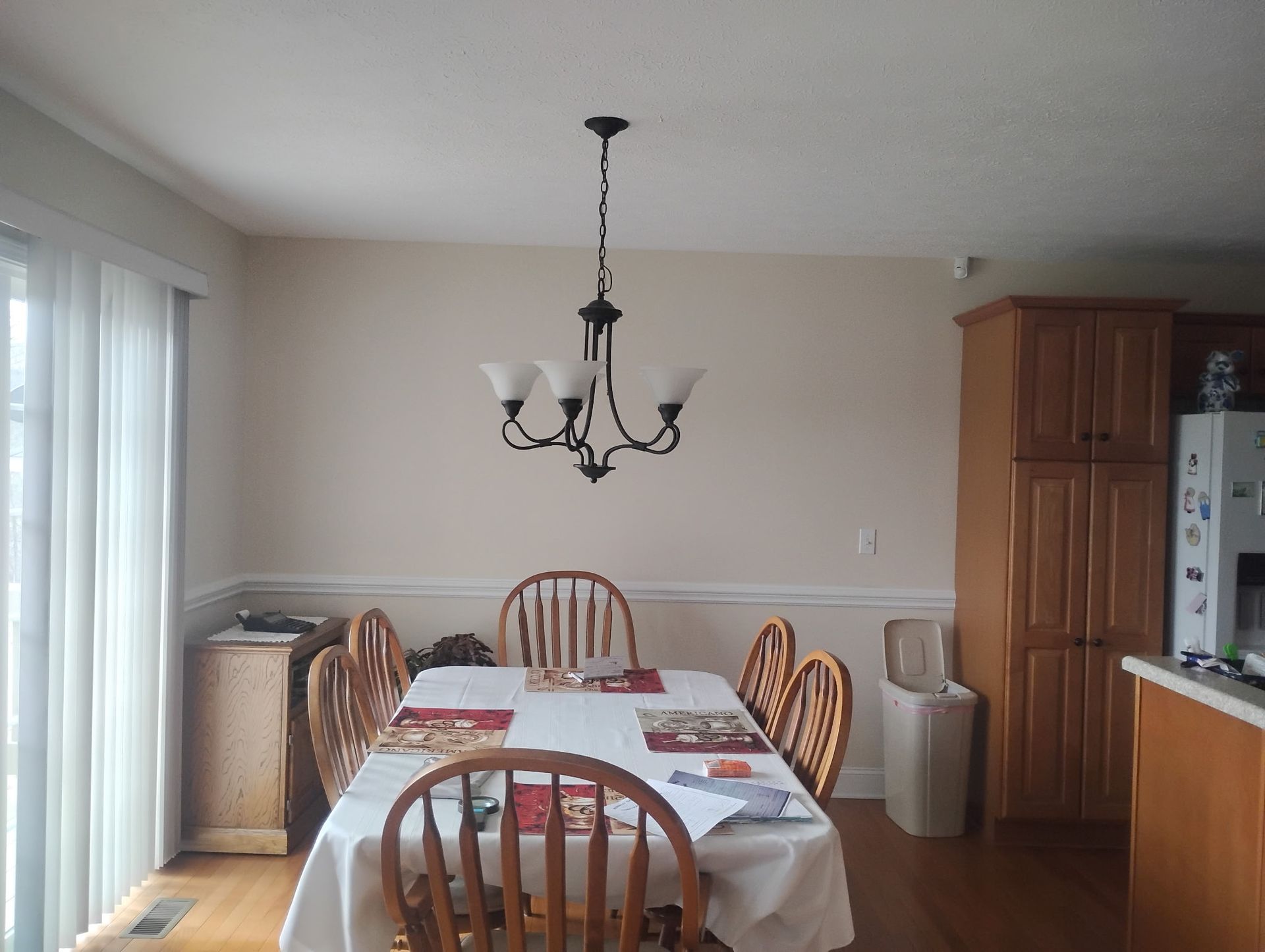 A dining area with a wooden table, chairs, and a hanging chandelier, situated near sliding glass doors and a pantry.