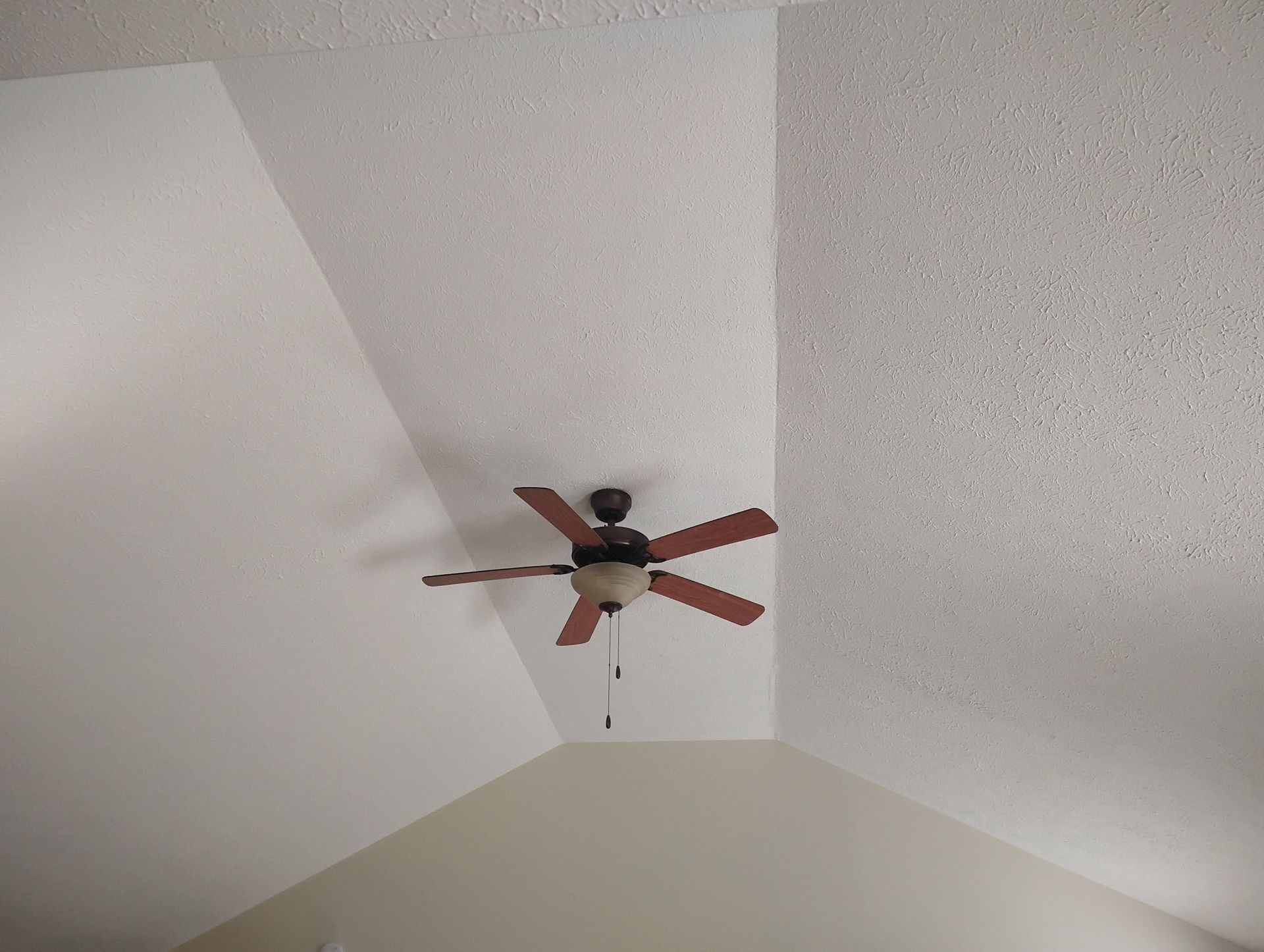 A ceiling fan with brown blades and a light fixture mounted on a sloped, textured ceiling.