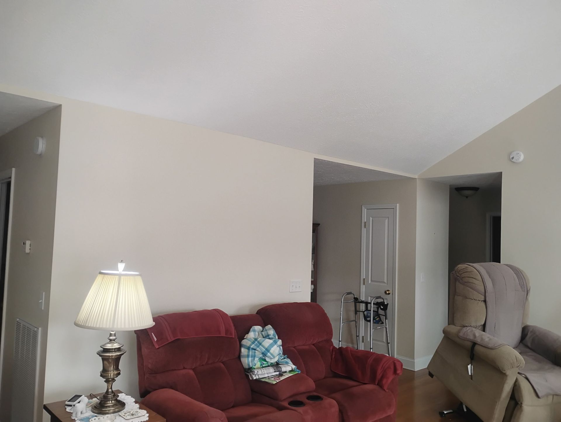 A red loveseat and a beige recliner in a living room with light-colored walls and a hallway in the background.