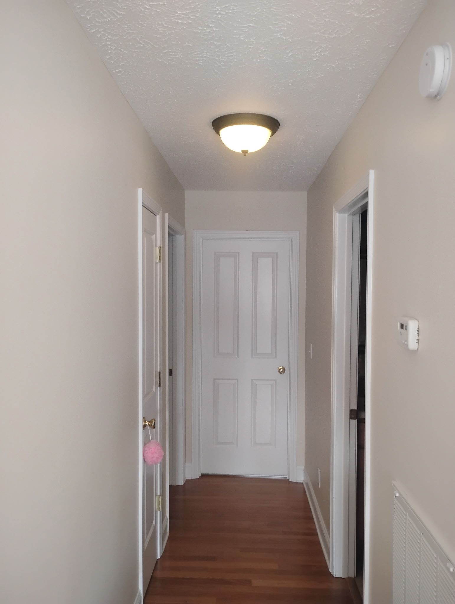 A brightly lit residential hallway with white walls, wood-look flooring, and white doors leading to other rooms.