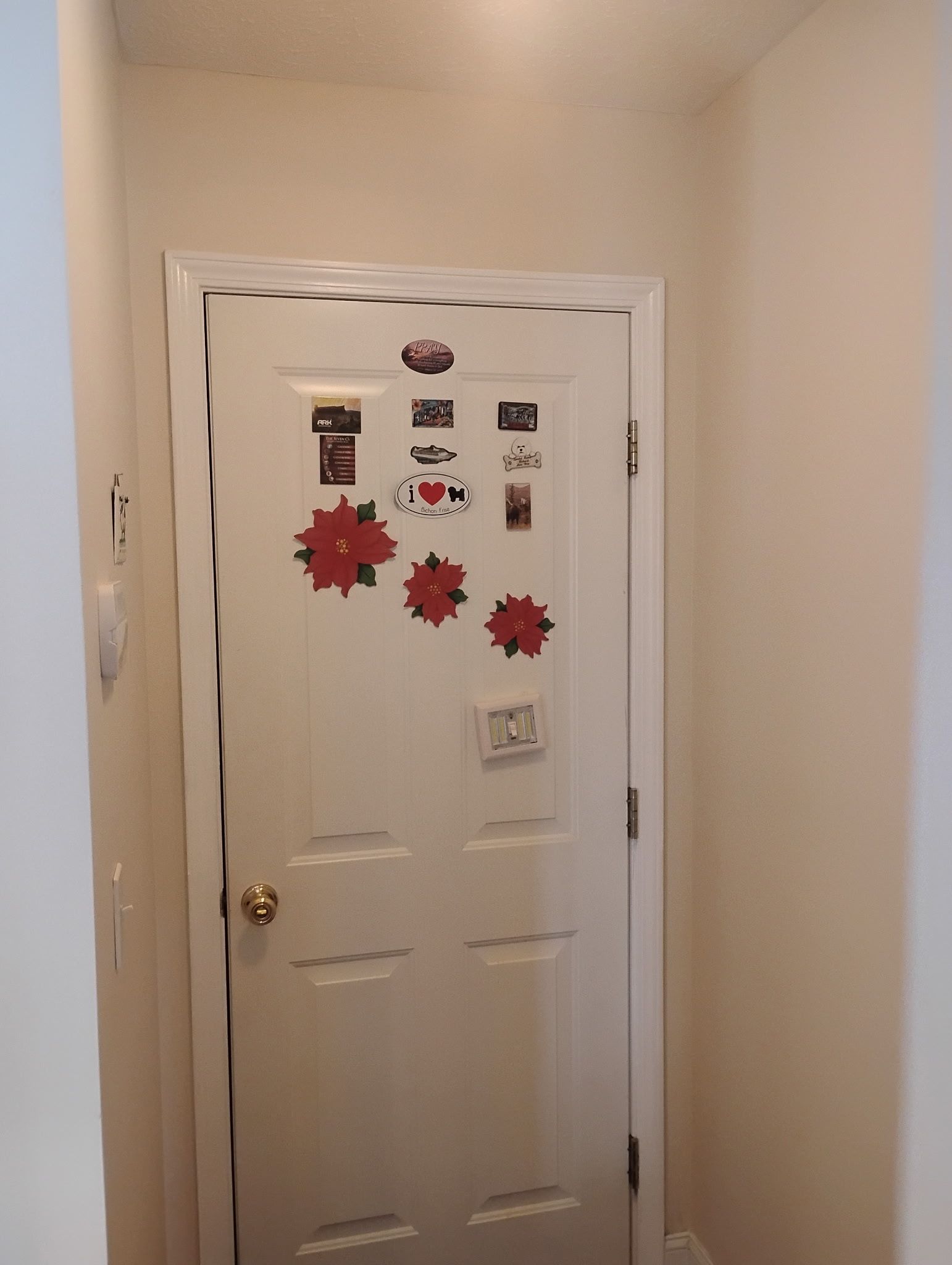 A white interior door decorated with three red poinsettia stickers and several small magnets in a hallway.