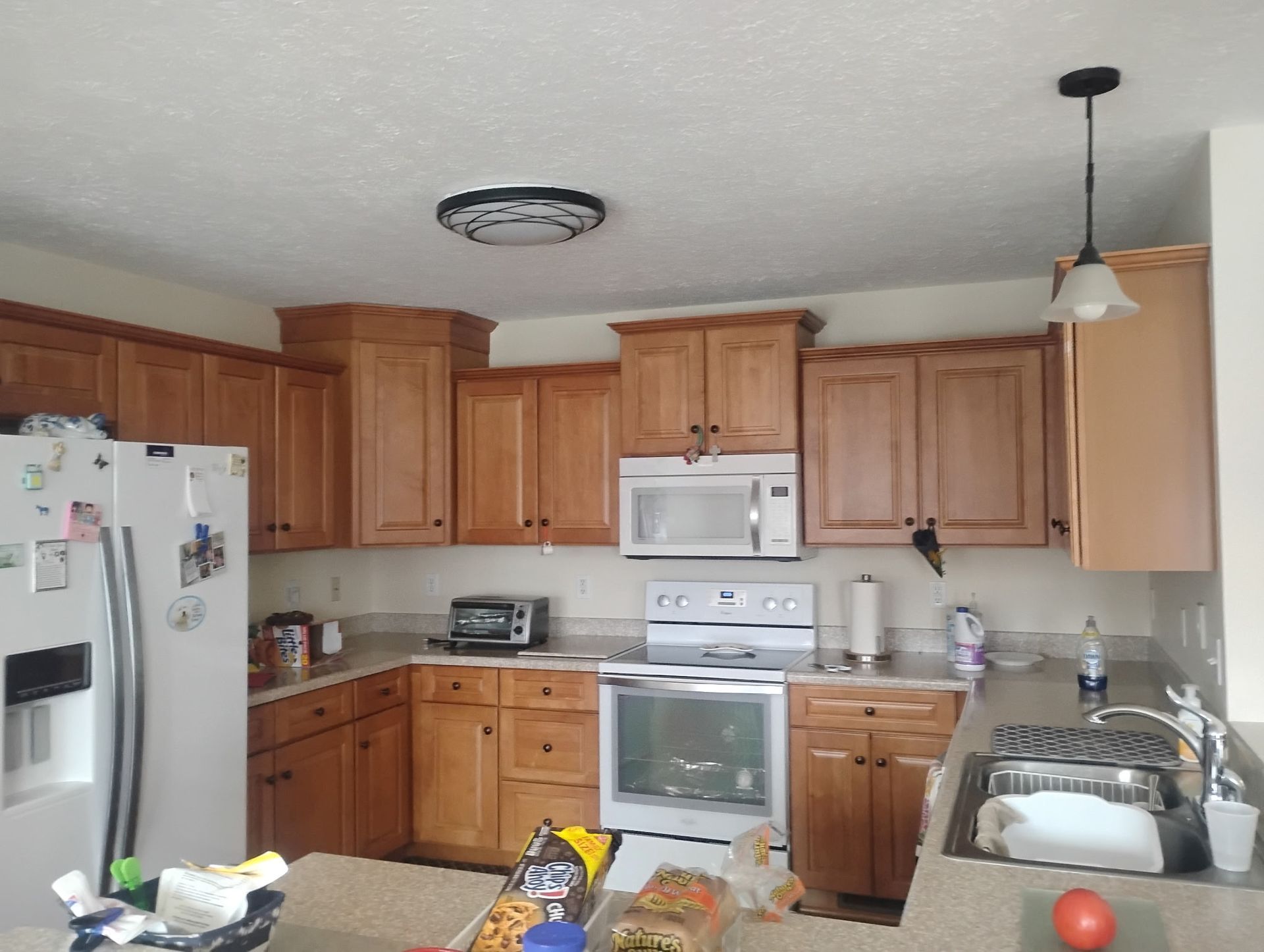 A kitchen with wood cabinets, white appliances, a light-colored countertop, and a hanging pendant light over the sink.